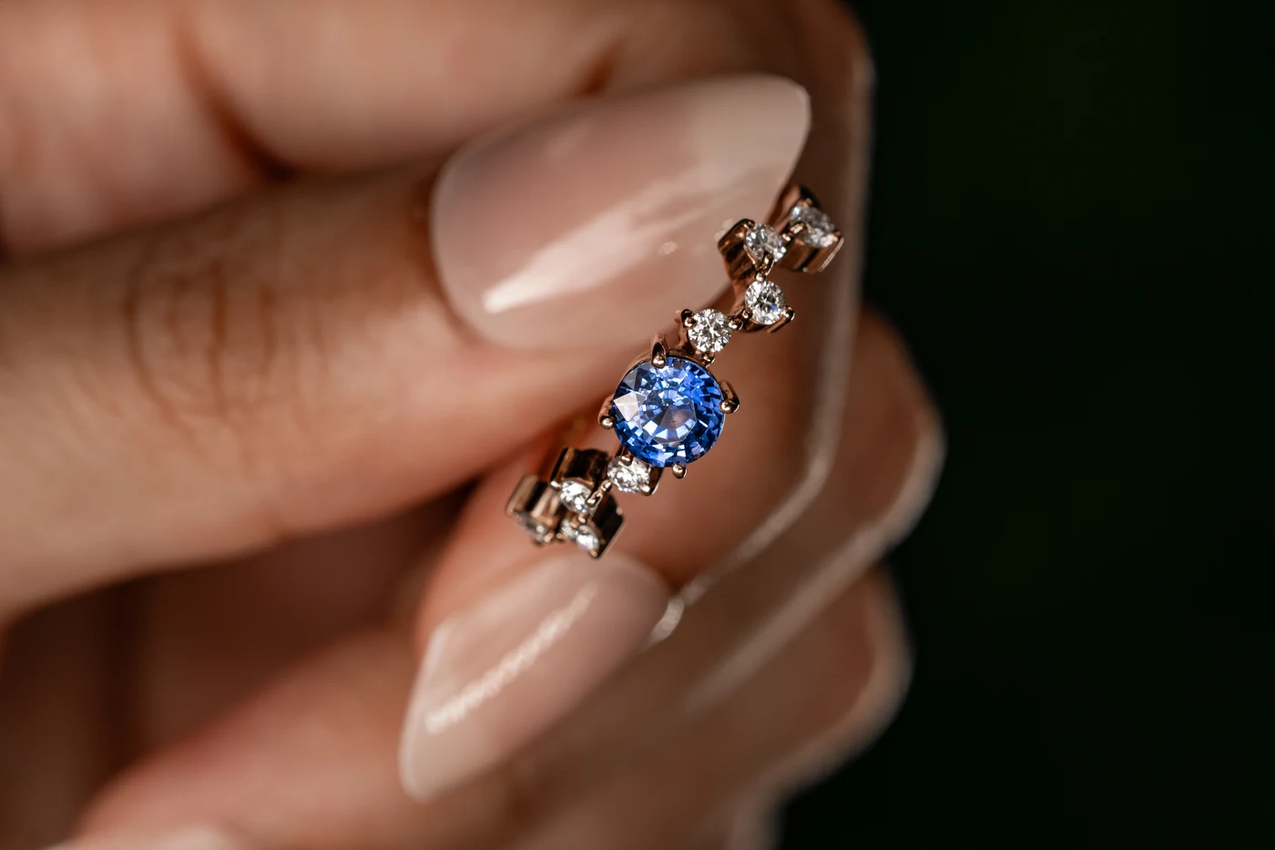 Close-up of an asymmetric rose gold ring with a blue sapphire and scattered diamonds