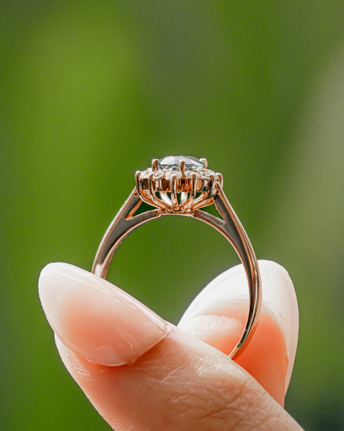 Rose gold sunburst halo ring held against green leaves