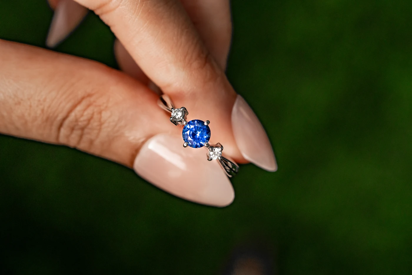 Round blue sapphire ring with diamond accents held between two fingers