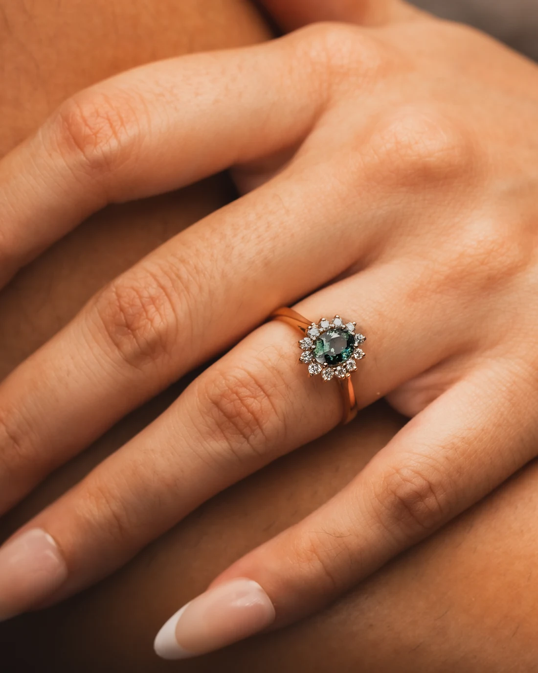Teal-green sapphire halo ring in rose gold worn on a hand